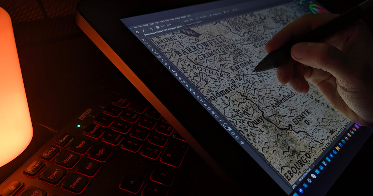 A close-up of a hand holding a stylus, using worldcrafter brushes to draw a detailed fantasy map on a tablet screen