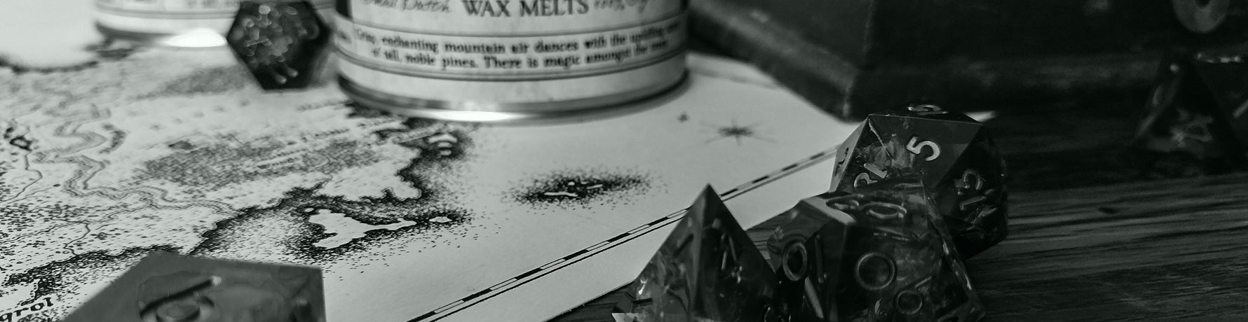 Dark and moody black and white photo of a fantasy map on desk with dice in the foreground
