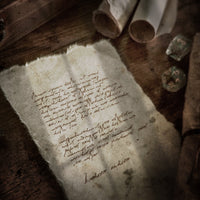 Promotional image used to advertise the free dungeons and dragons font called garbled hand, an old mysterious note sits on a desk with dice and scrolls