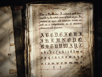 An old book sits open and is filled with old calligraphy, used to promote the Spellbinder font by Aesoterik