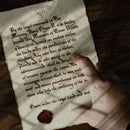 Image of a physical letter prop created for a ttrpg campaign, a player points at medieval calligraphy writing on an ancient looking note