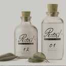 An advert for a fictional brand called Petal, showing Two old, clear, apothecary style glass bottles with cork lids, containing an essential oil