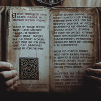 Promotional image for the Mercian Quill font, it is a digital manipulated photograph showing a medieval figure holding out a book to the viewer. The book is filled with writing that appear from anglo-saxon times.